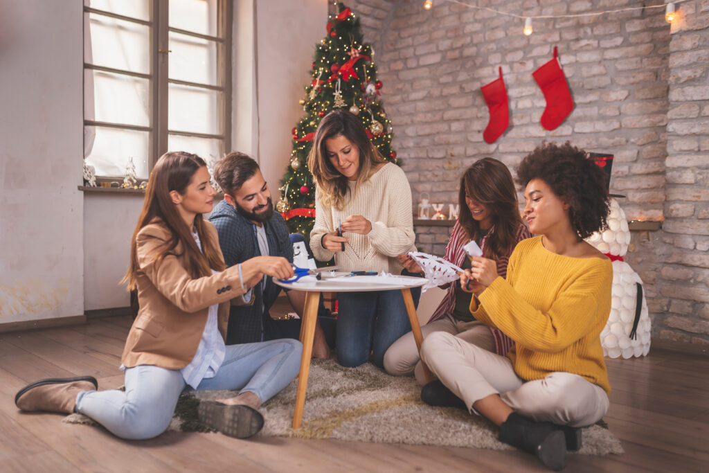 Friends having fun while making Christmas decorations, cutting out paper snowflakes