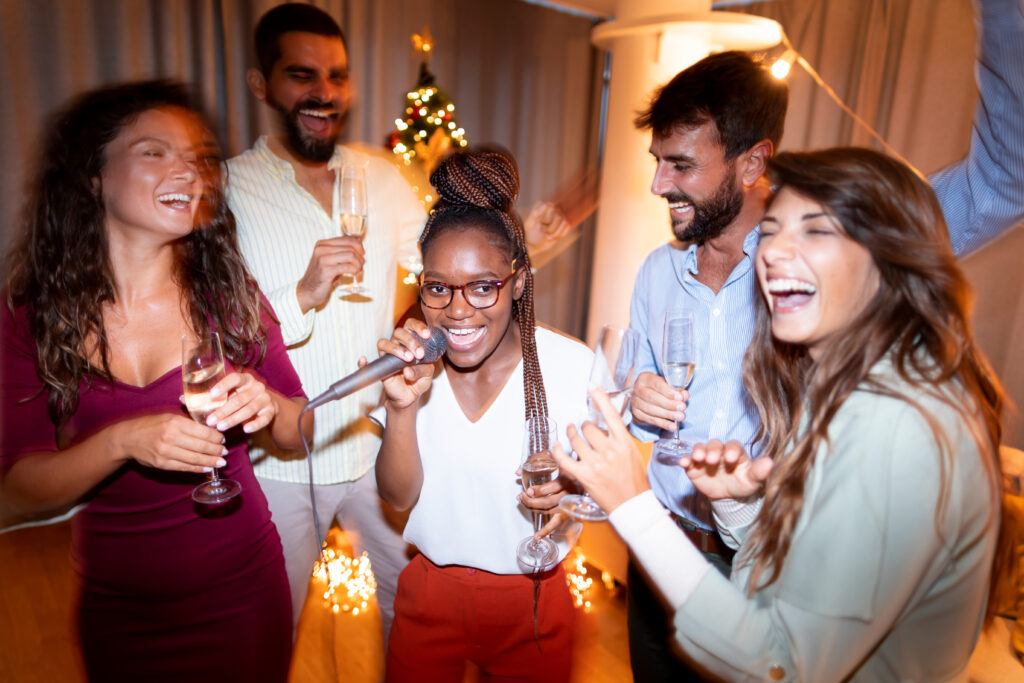 Group of cheerful young friends having fun at late night party, singing karaoke, dancing and drinking champagne