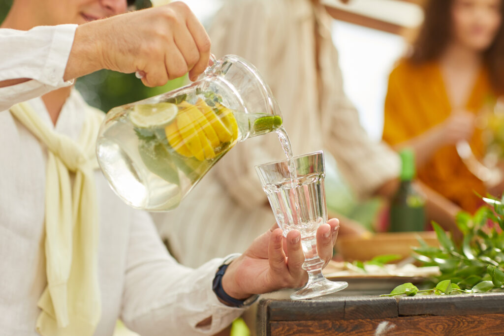 Close up of a man pouring lemonade into glass cup while enjoying outdoor party in Summer.