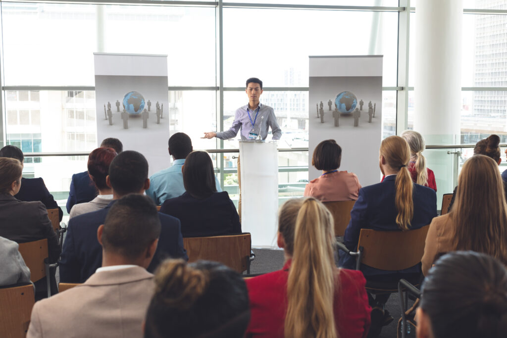 Front view of young man speaking in front of diverse group of people at seminar