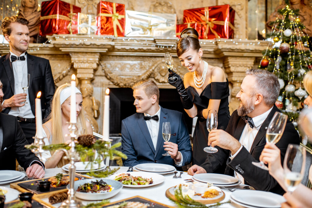 Elegantly dressed group of people having fun, clinking wine glasses during a festive dinner near the fireplace and christmas tree, celebrating the holidays