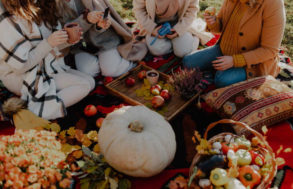 A group of friends having an autumn picnic with different vegetables, fruits and tea, on a blanket