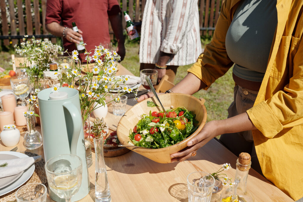 Young woman placing a spring salad on a table with drinks and wildflowers