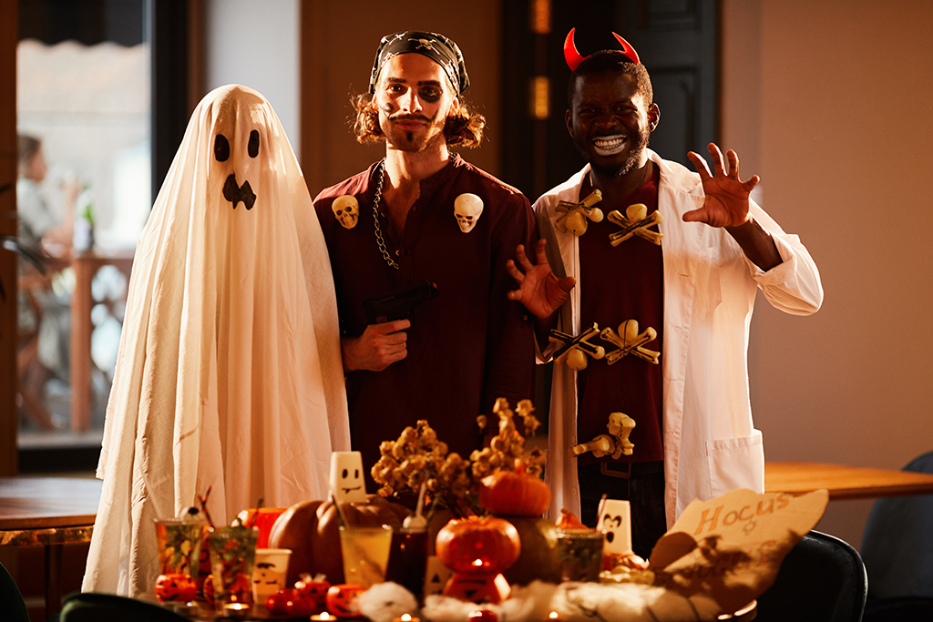 Portrait of three people wearing Halloween costumes posing by decorated table during party