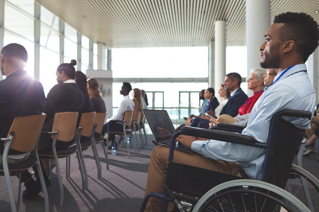 Side view of young businessman, wheelchair user with a laptop during seminar in office building